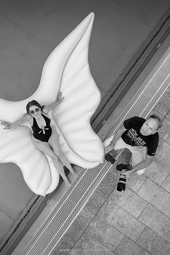 Andreas Schnitzlhuber fotografiert von oben eine Frau auf aufblasbaren Engelsflügeln am Pool, schwarz-weiß