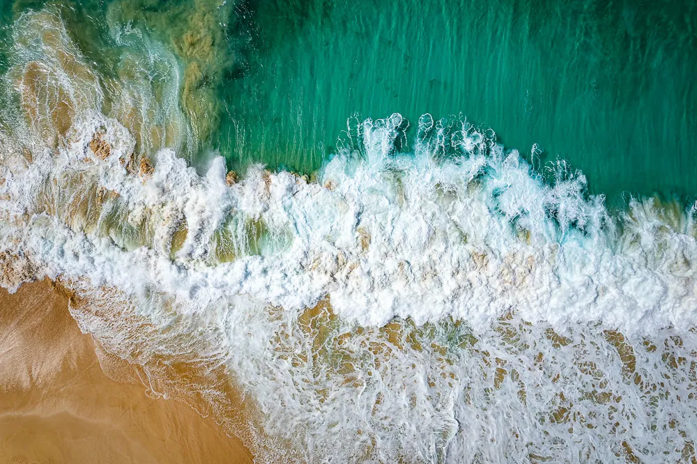 Wellen brechen an einem goldenen Strand, von oben